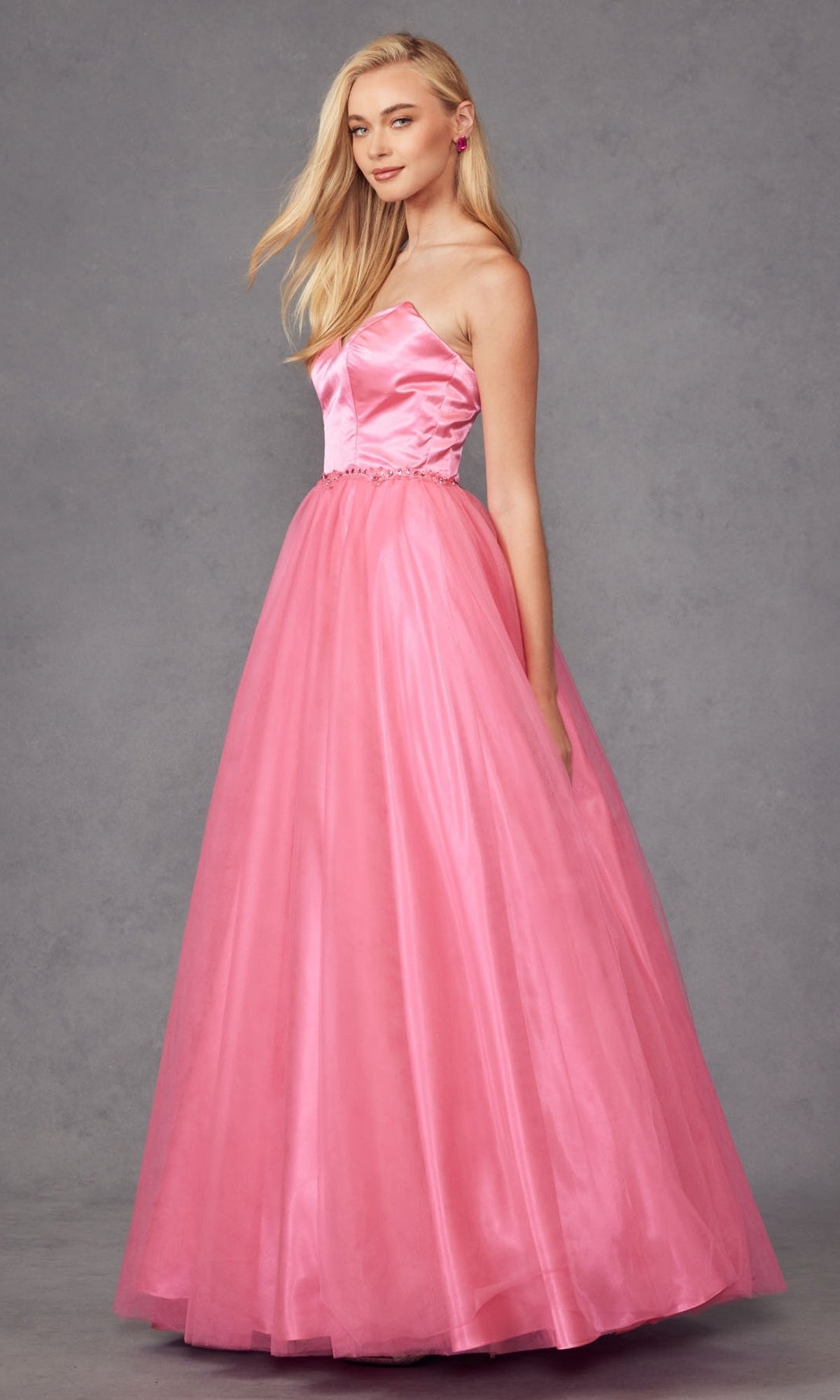 A woman in the Strapless Sweetheart Long Prom Ball Gown 265, featuring a fitted satin bodice, corset back, and full tulle skirt, stands against a plain gray background. The floor-length pink dress exudes timeless elegance.